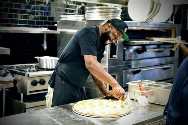 man-wearing-black-clothing-making-pizza-restaurant-kitchen