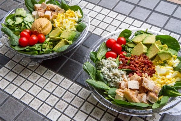 2-salads-in-plastic-bowls-on-grey-tiled-table