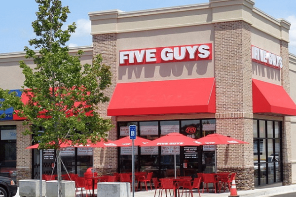 five-guys-red-sign-outside-building-red-umbrellas-chairs-tables-and-trees
