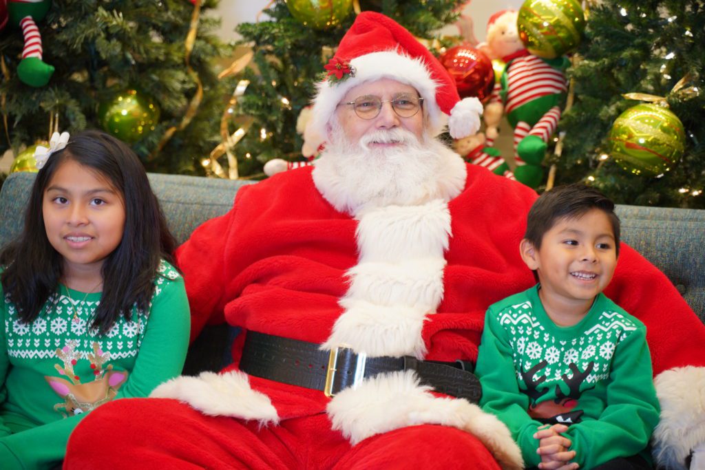 santa sitting with two children on either side of him 