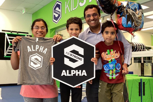 A family at KidStrong holding an Alpha sign