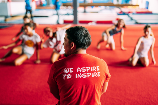 dominique_dawes_4 gymnastics coach wearing a red shortsleeve shirt that says "we aspire to inspire"